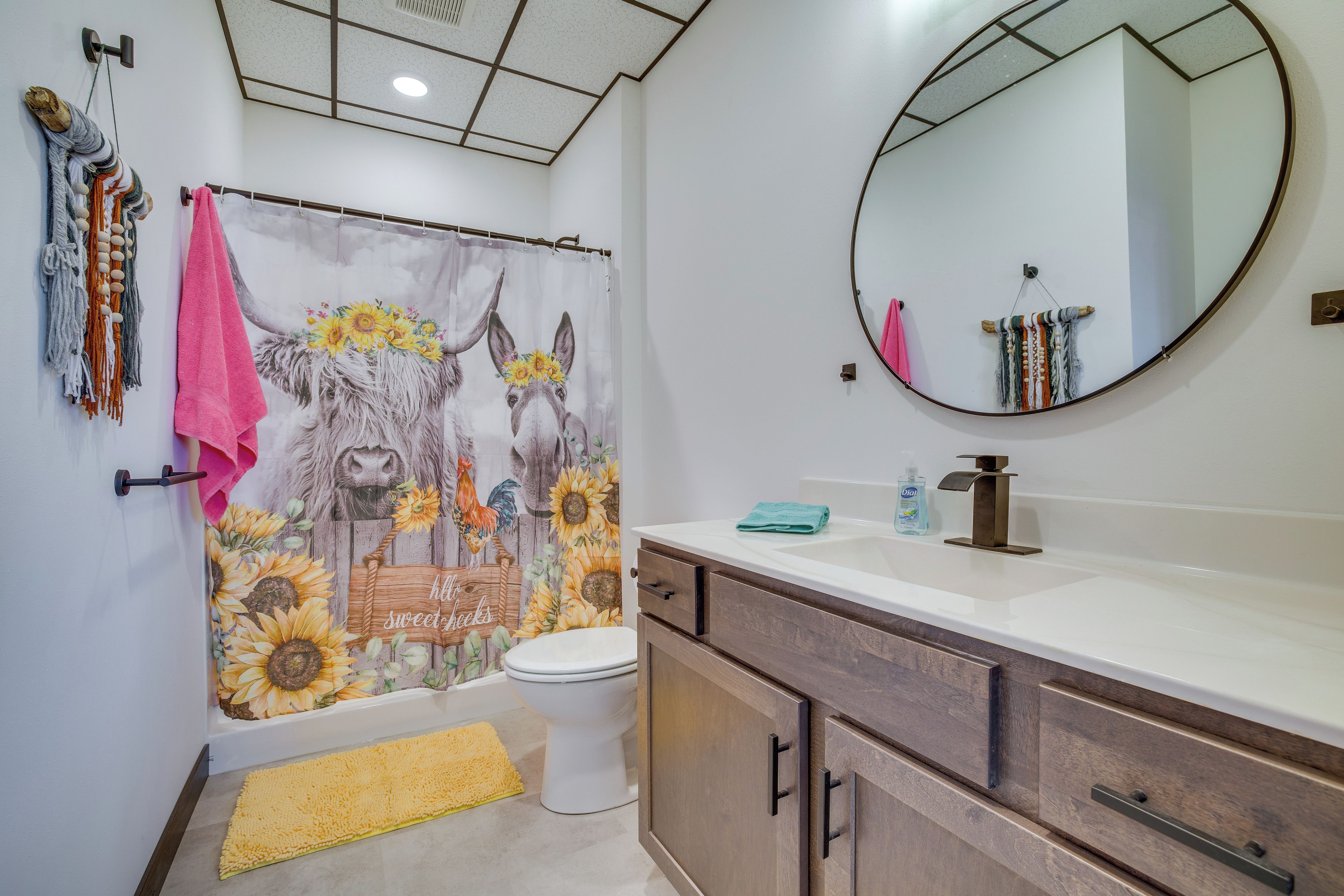 Une salle de bain avec un rideau de douche orné de motifs floraux, des toilettes, un lavabo avec un miroir et des meubles en bois.