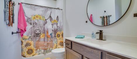 Une salle de bain avec un rideau de douche orné de motifs floraux, des toilettes, un lavabo avec un miroir et des meubles en bois.