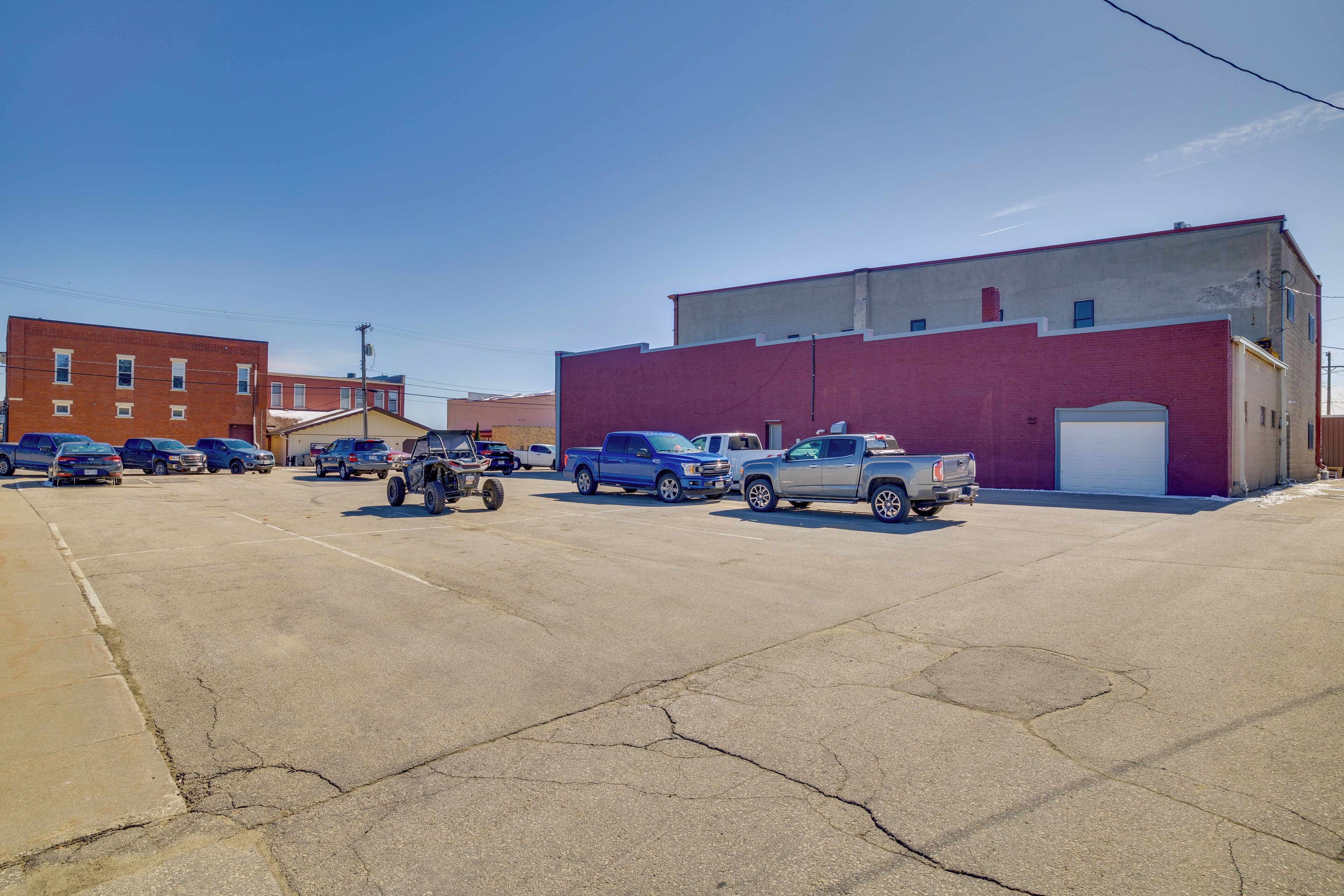 A parking lot with several vehicles, including trucks and cars, parked in front of a red brick building with a white garage door.