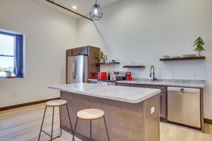 A modern kitchen with a central island, stainless steel appliances, and wooden bar stools. - Cashton Studio Apartment: Steps to Downtown! (Cashton)