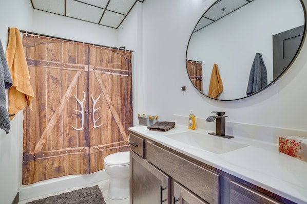 A bathroom with a wooden shower curtain, a white toilet, a sink with a mirror, and towels hanging on the wall.
