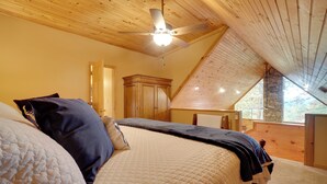 A bedroom with a wooden ceiling, a bed with a quilted cover, a nightstand, and a window with a view of the outdoors. - Picturesque Clayton Cabin w/ Mountain Views! (Clayton)