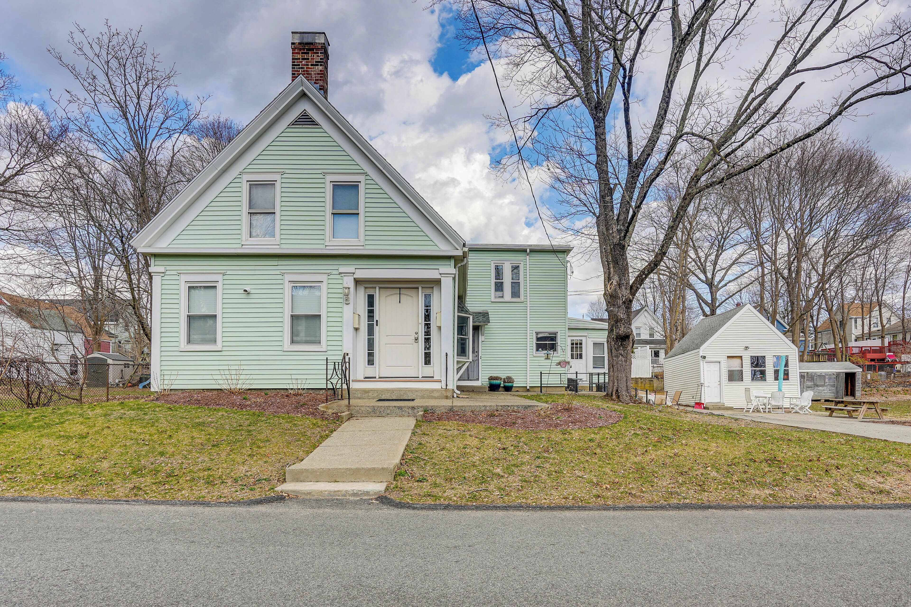 A two-story house with a front porch, a small attached garage, and a yard with a lawn and trees.