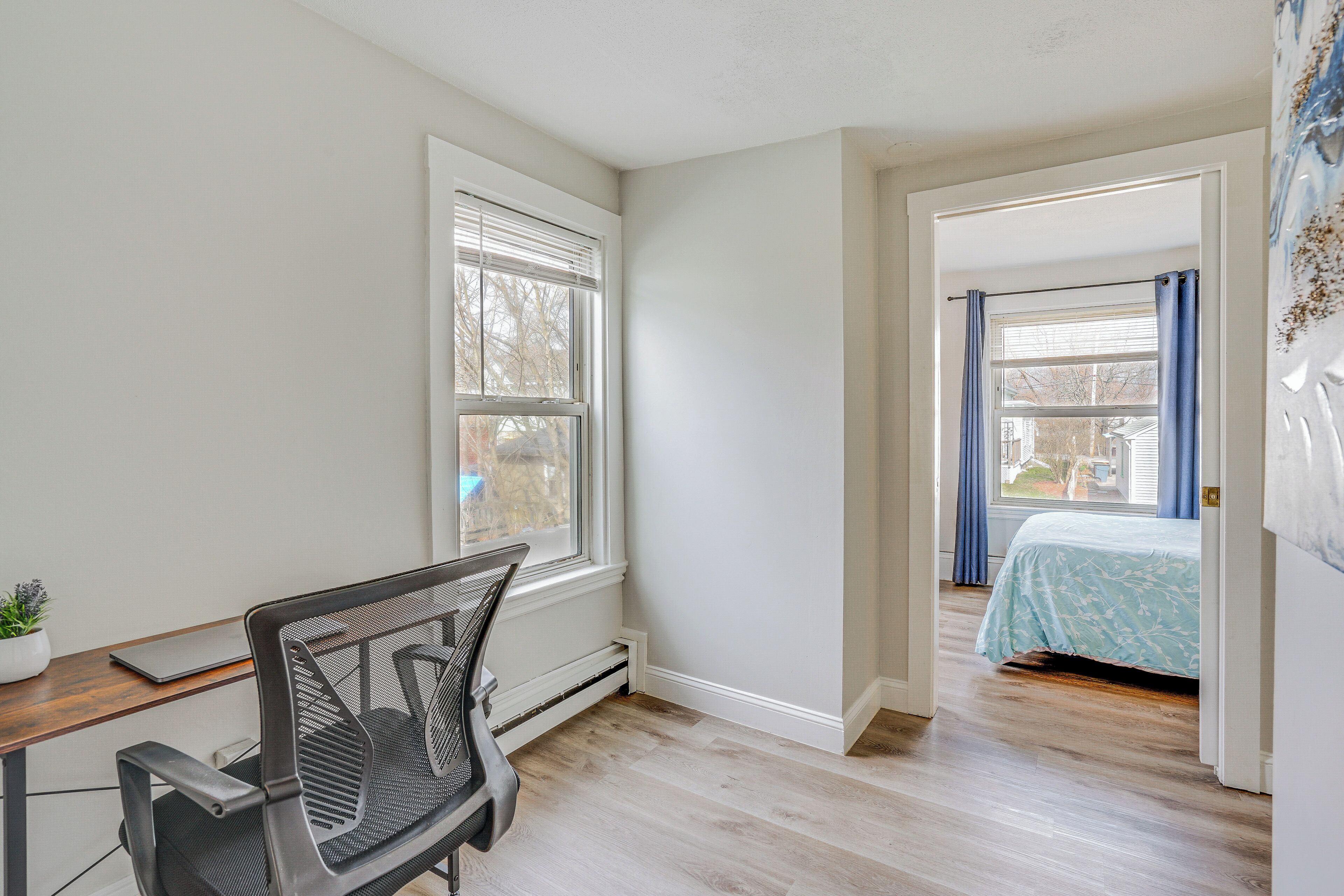 Een kamer met een bureau, stoel en een bed met een blauw dekbed.