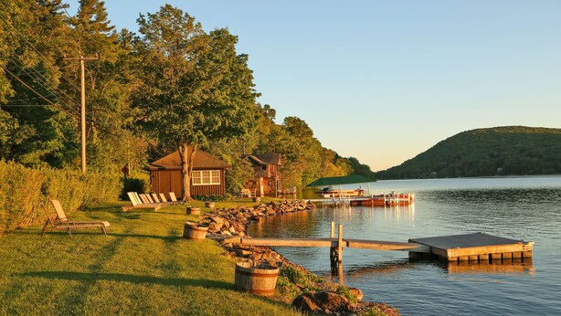 A lakeside property with a dock, a grassy area with lounge chairs, and a small cabin. - Grand Lakefront Home in Warren w/ Expansive Patio! (New Preston)