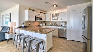 A modern kitchen with white cabinetry, a granite countertop, stainless steel appliances, and a built-in island with bar stools. - Surfside Beach Home w/ Deck on Pedestrian Beach! (Freeport)