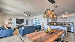 A spacious living room with a wooden dining table, blue sofas, and a kitchen area with white cabinets and stainless steel appliances. - Surfside Beach Home w/ Deck on Pedestrian Beach! (Freeport)