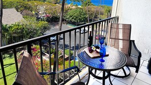 A balcony with a view of the ocean, a table with a bottle and a glass, and a chair. - Bright Kihei Renovated Condo New AC Steps to Kamaole II Beach and Pool (Kihei)
