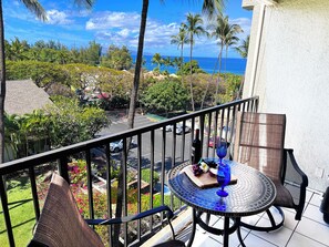A balcony with a view of the ocean, a table with a bottle and a glass, and a chair.