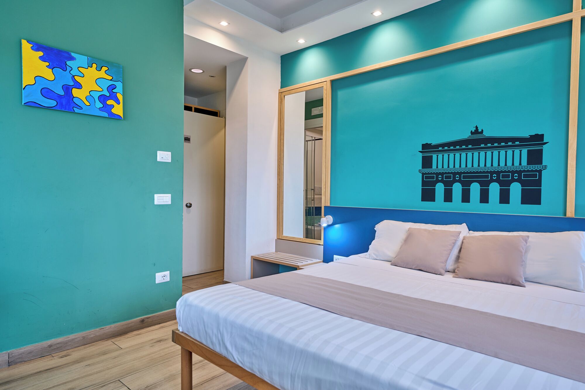 A bedroom with a bed, a wall painting, and a large mirror.