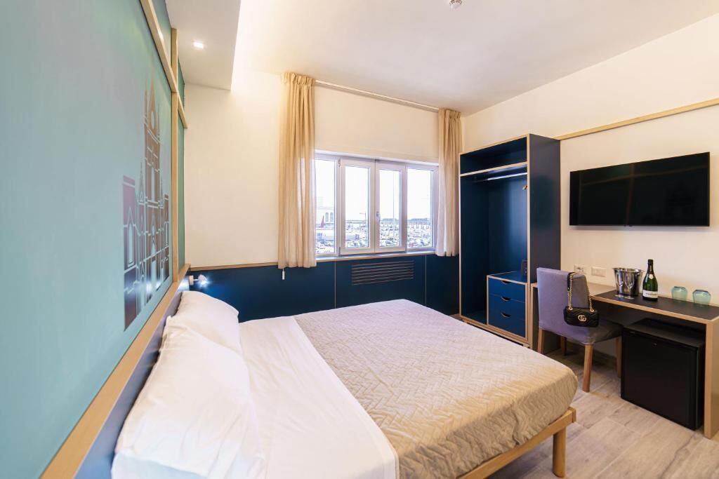 A hotel room with a bed, a desk, a chair, a TV, and a window with curtains.