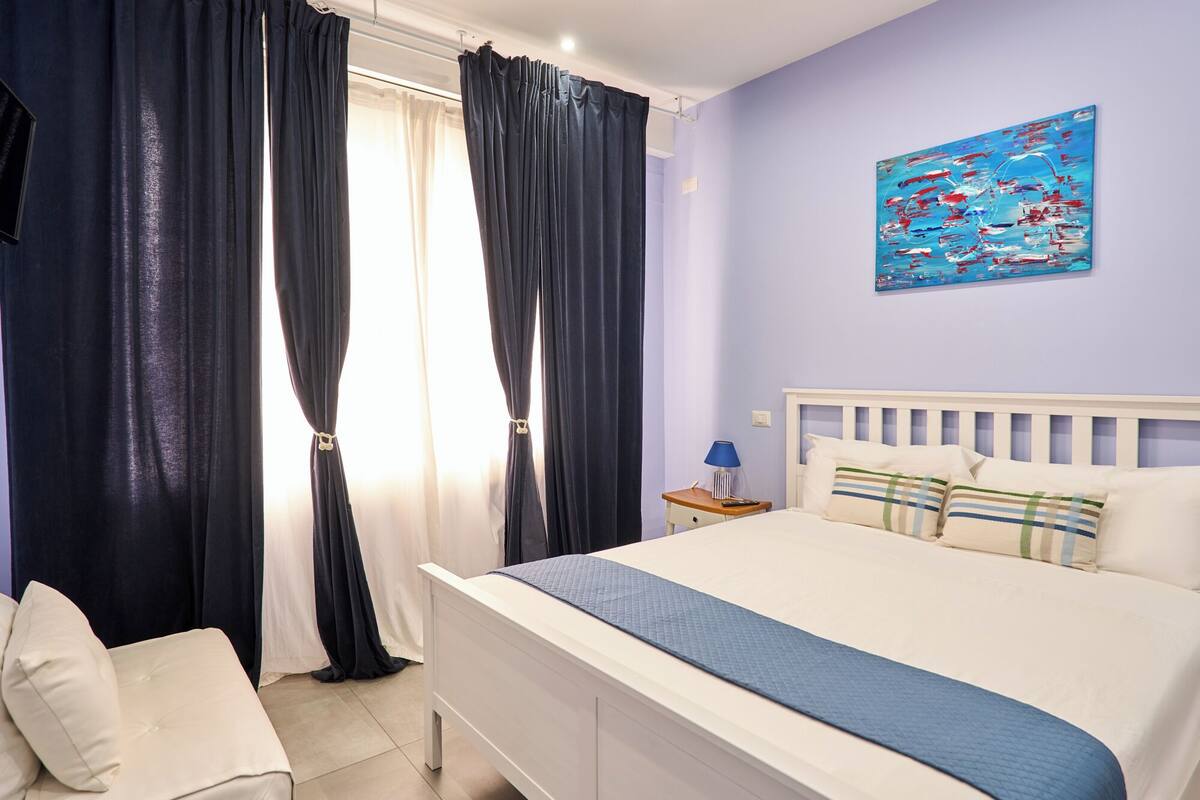 A bedroom with a bed, a nightstand, a lamp, and a painting on the wall.