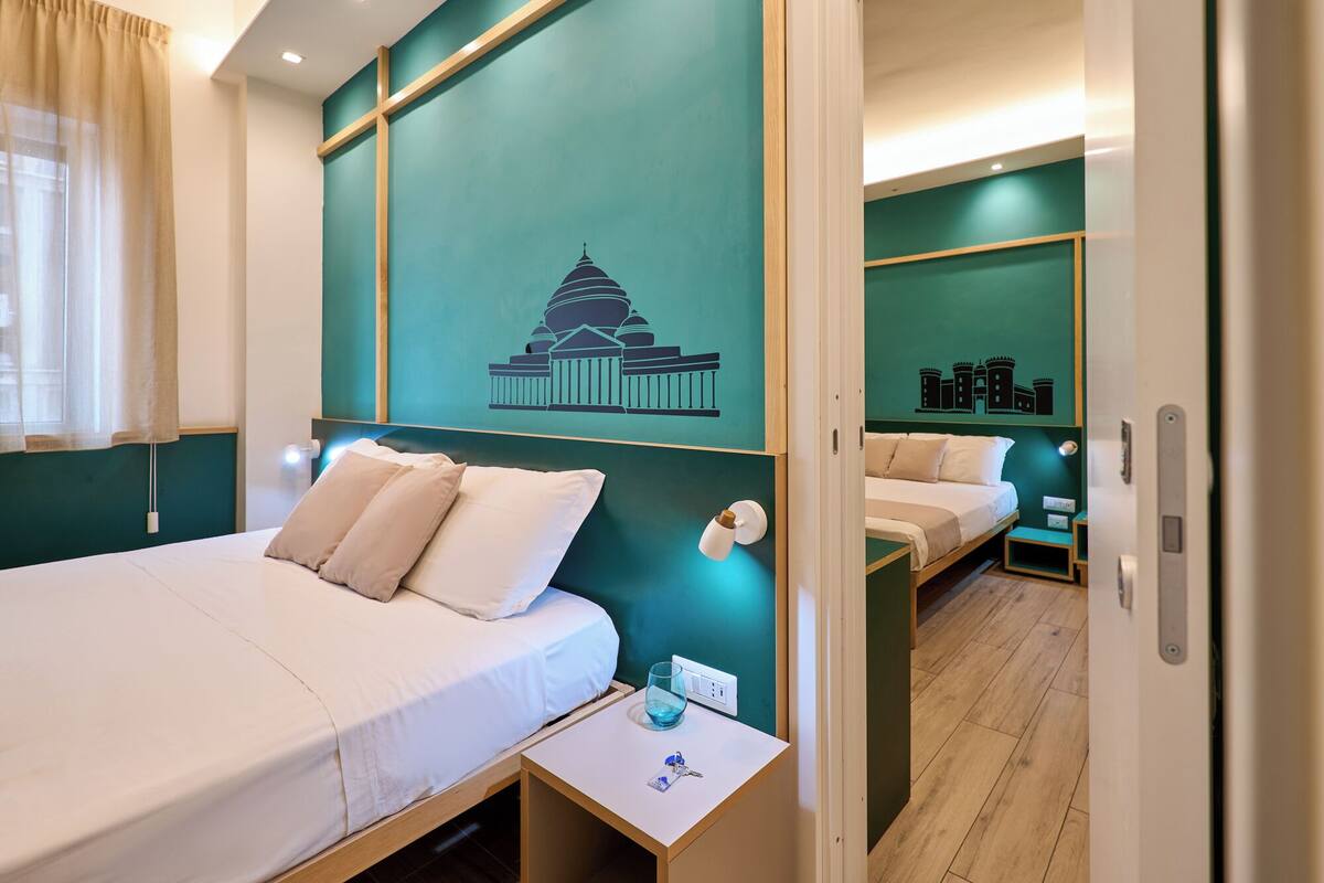 A hotel room with two beds, a nightstand with a glass of water, and a wall with a cityscape mural.