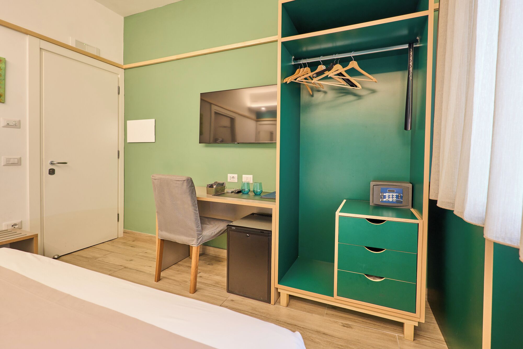 A hotel room with a bed, a desk, a chair, a wardrobe, and a small cabinet.