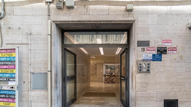 A hotel entrance with a glass door, a reception desk inside, and various signs on the wall indicating services like digital printing and photo printing. - La Marina (Naples)