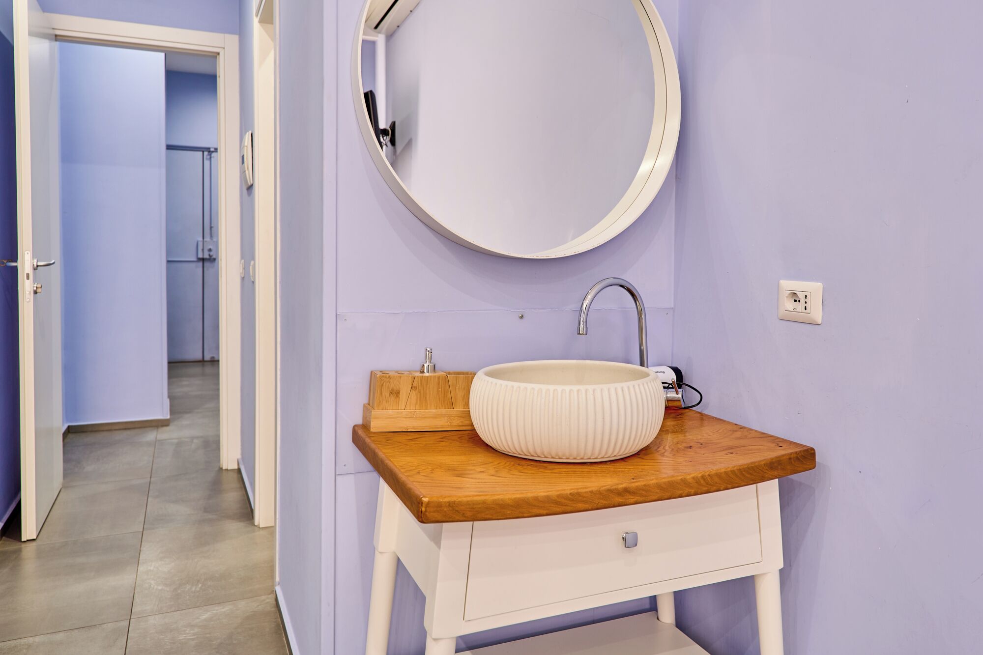 Un baño con un espejo redondo, un lavabo blanco y una encimera de madera.