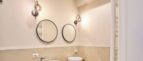 Une salle de bain moderne avec deux miroirs ronds, un lavabo blanc et un sèche-cheveux posé sur le comptoir.