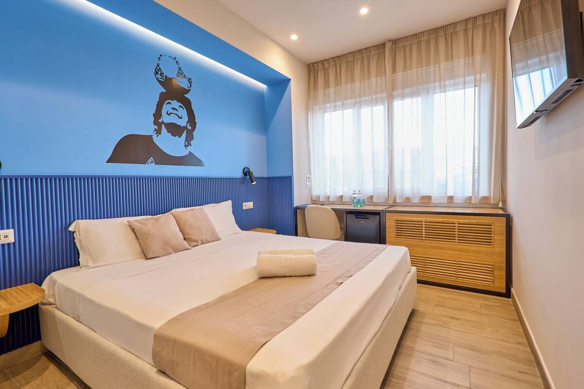 A hotel room with a large bed, a desk, and a window with curtains.