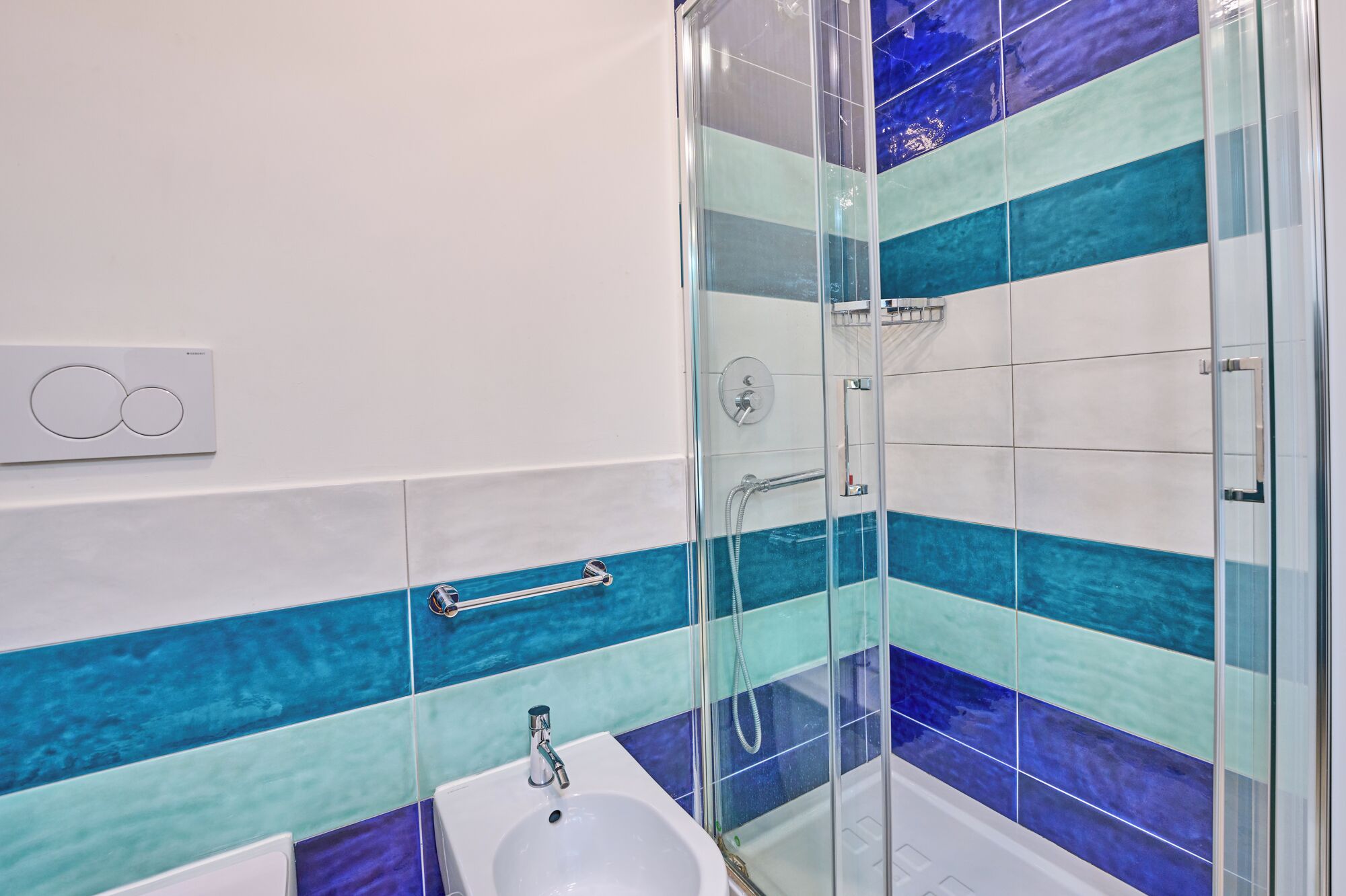 Un baño con ducha de vidrio, lavamanos blanco y un perchero para toallas.