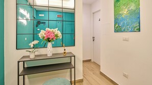A hallway with a teal-colored wall, a mirror, a vase with flowers, a small table, and a painting. - La Marina (Naples)