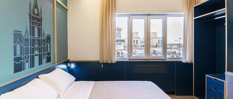 Habitación de hotel con una cama grande, una ventana con cortinas, un armario y vistas a la ciudad.