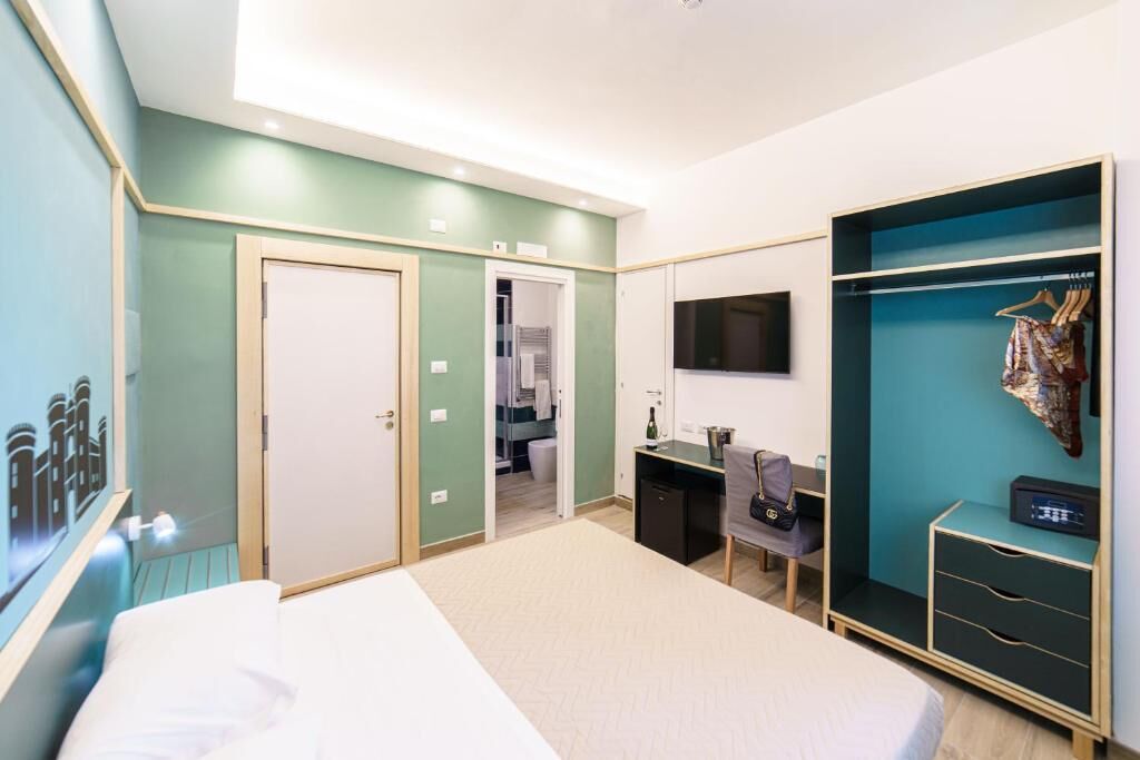 Une chambre d’hôtel avec un lit, un bureau, une armoire, une télévision et une salle de bain visible à travers une porte ouverte.