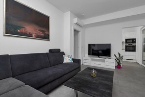 A modern living room with a dark grey sofa, a flat-screen TV, and a coffee table with a glass vase.