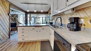 A modern kitchen with wooden flooring, white cabinets, a central island, and a coffee maker. - Spacious Slopeside Location by RedAwning (Mammoth Lakes)
