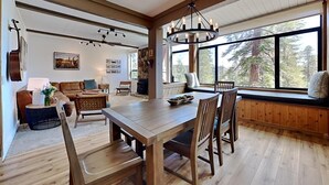 A spacious living area with a wooden dining table, comfortable seating, and large windows offering a view of the outdoors. - Spacious Slopeside Location by RedAwning (Mammoth Lakes)