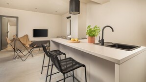 A modern kitchen with a large island, black bar stools, a potted plant, and a flat-screen TV mounted on the wall.