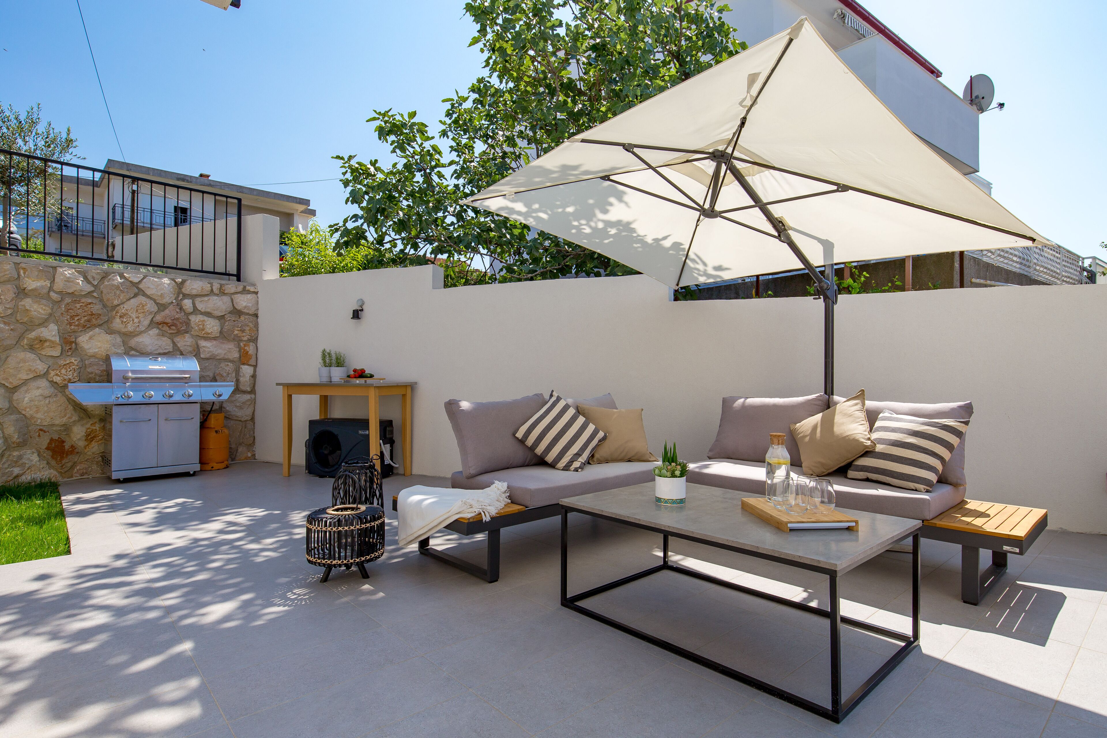 Een overdekt terras met een bank, bijzettafeltje en parasol.