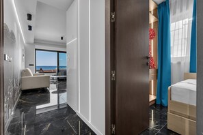 Et moderne hotelværelse med et stort vindue der udgiver udsigt til havet, en balkon og en pænt redt seng med et blåt gardin.