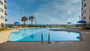 Une piscine entourée d’une clôture et de palmiers, avec des chaises longues et des parasols.