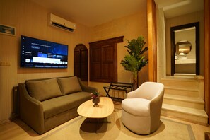 Un salon comprenant un canapé, un fauteuil, une table basse, un téléviseur et une plante.