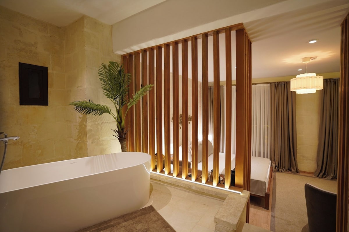 Un baño moderno con una bañera independiente, una planta en maceta y un separador de madera.
