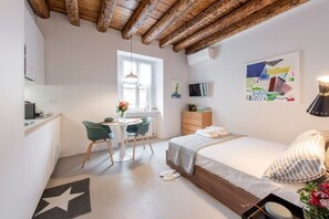 Ein modernes Schlafzimmer mit Bett, Schreibtisch und Stuhl. Ein Fenster, ein Fernseher und ein Gemälde sind an der Wand zu sehen.