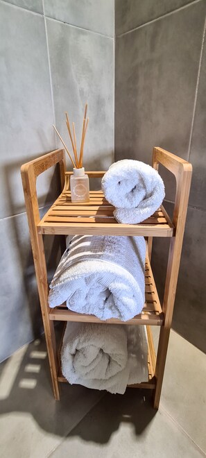 Una estantería de madera con dos toallas blancas y un difusor de aroma de juncos en un baño.