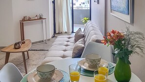A modern living room with a sofa, dining table set with plates, glasses, and a vase of flowers. - Lux Apart Cba (Córdoba)