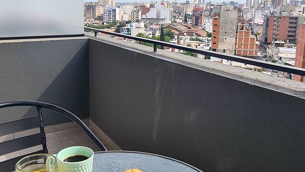 A balcony with a table set for breakfast, including croissants and orange juice, overlooking a cityscape. - Lux Apart Cba (Córdoba)