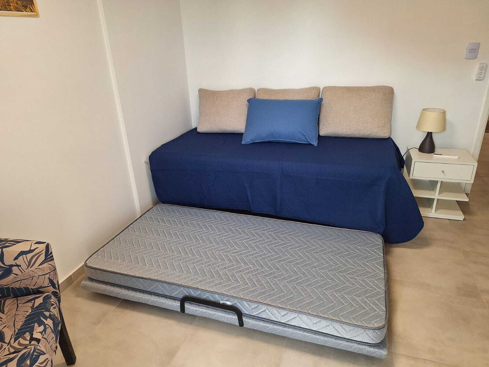 Une chambre à coucher avec un lit, une table de chevet avec une lampe et une valise posée sur le sol.