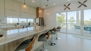 A modern kitchen with a large island, pendant lights, and a view to the outdoors.