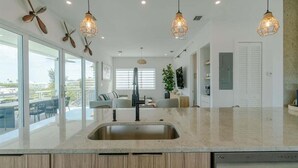 A modern kitchen with a large island, pendant lights, and a view to the outside.