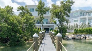 A wooden bridge leading to a modern building with multiple floors and large windows. - Paraiso Del Mar~ Luxury Tropical Oasis, 65' Dock, Pet Friendly! (Marathon)