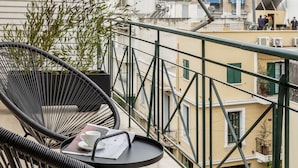 Un balcon avec deux fauteuils en osier noir, une petite table ronde et un pot de fleurs.