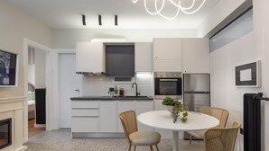 Une cuisine moderne avec des meubles blancs, une table de salle à manger ronde, des chaises en osier et un four encastré.