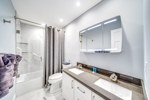 A modern bathroom with a glass shower enclosure, a white toilet, a vanity with two sinks, and a large mirror. - Heated Pool+Waterfront! Golf Cart+1 Mile To Beach! (Fort Lauderdale)