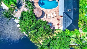 Vue aérienne d’un complexe hôtelier doté d’une piscine, de chaises longues et d’un aménagement paysager de style tropical.