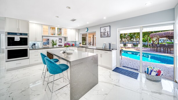 Une cuisine moderne dotée d’un îlot central, de meubles blancs et offrant une vue sur une piscine.