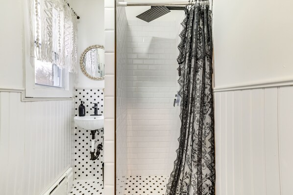 Un bagno con un lavandino bianco, uno specchio e una doccia dotata di tenda decorata.