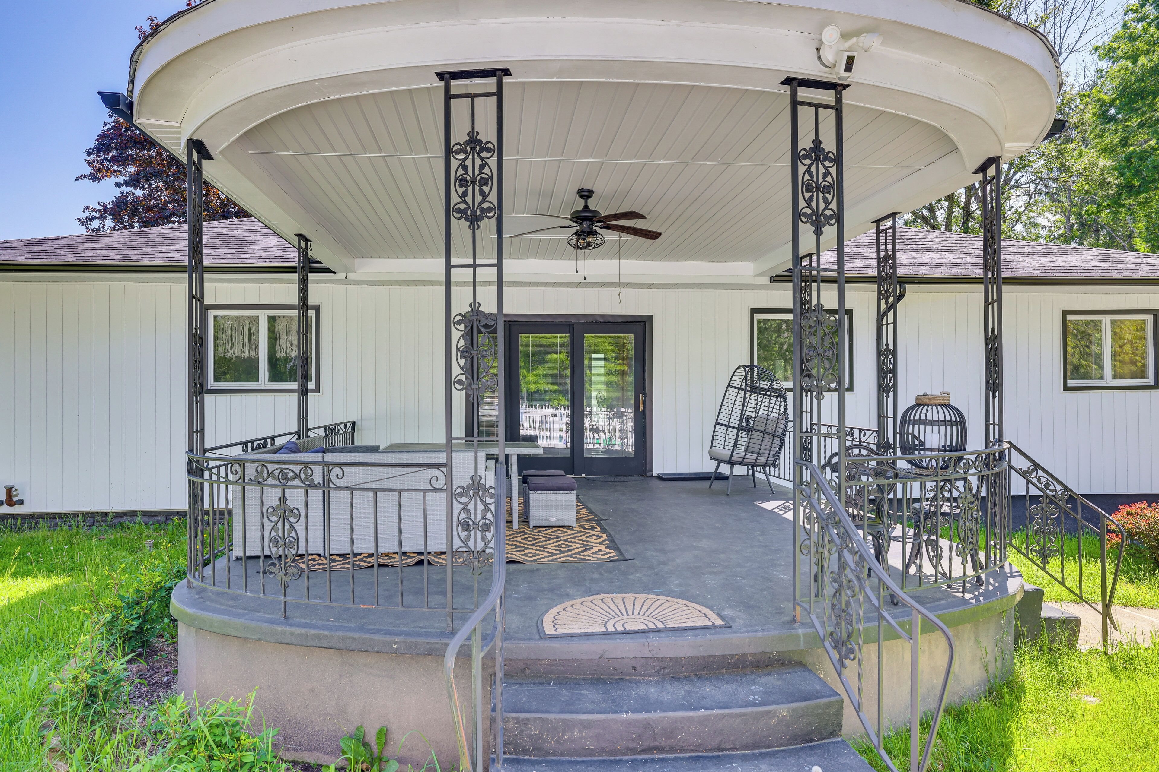 A covered outdoor area with a curved roof, a central seating area with chairs and a table, and a staircase leading to the entrance.